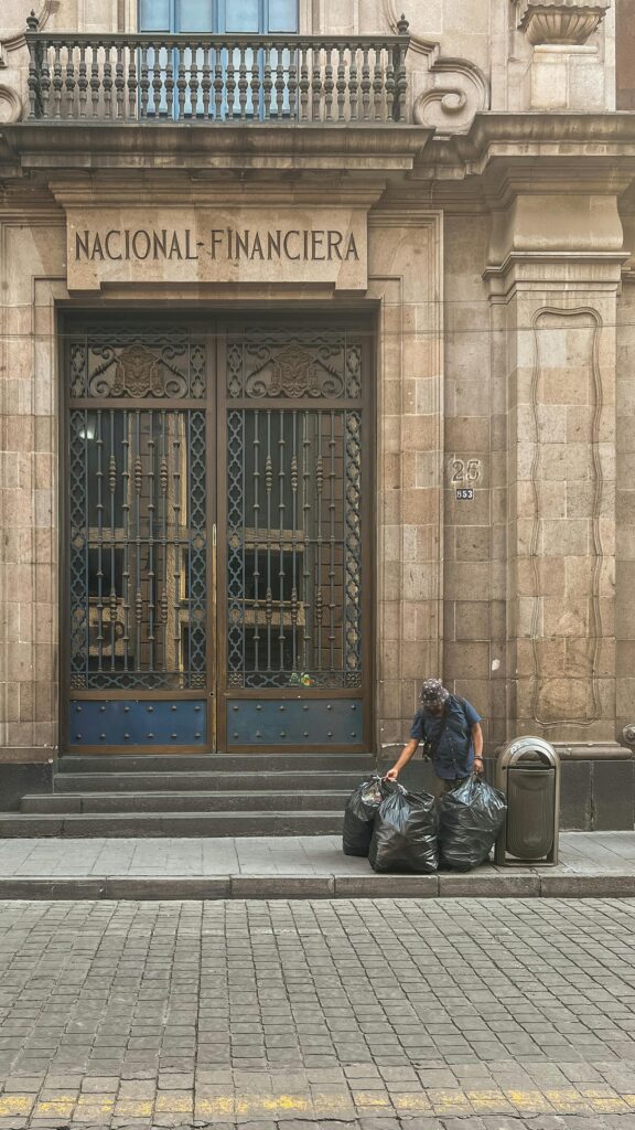 pexels-photo-16466108-16466108 Worker arranging trash bags outside historic urban building Nacional Financiera.